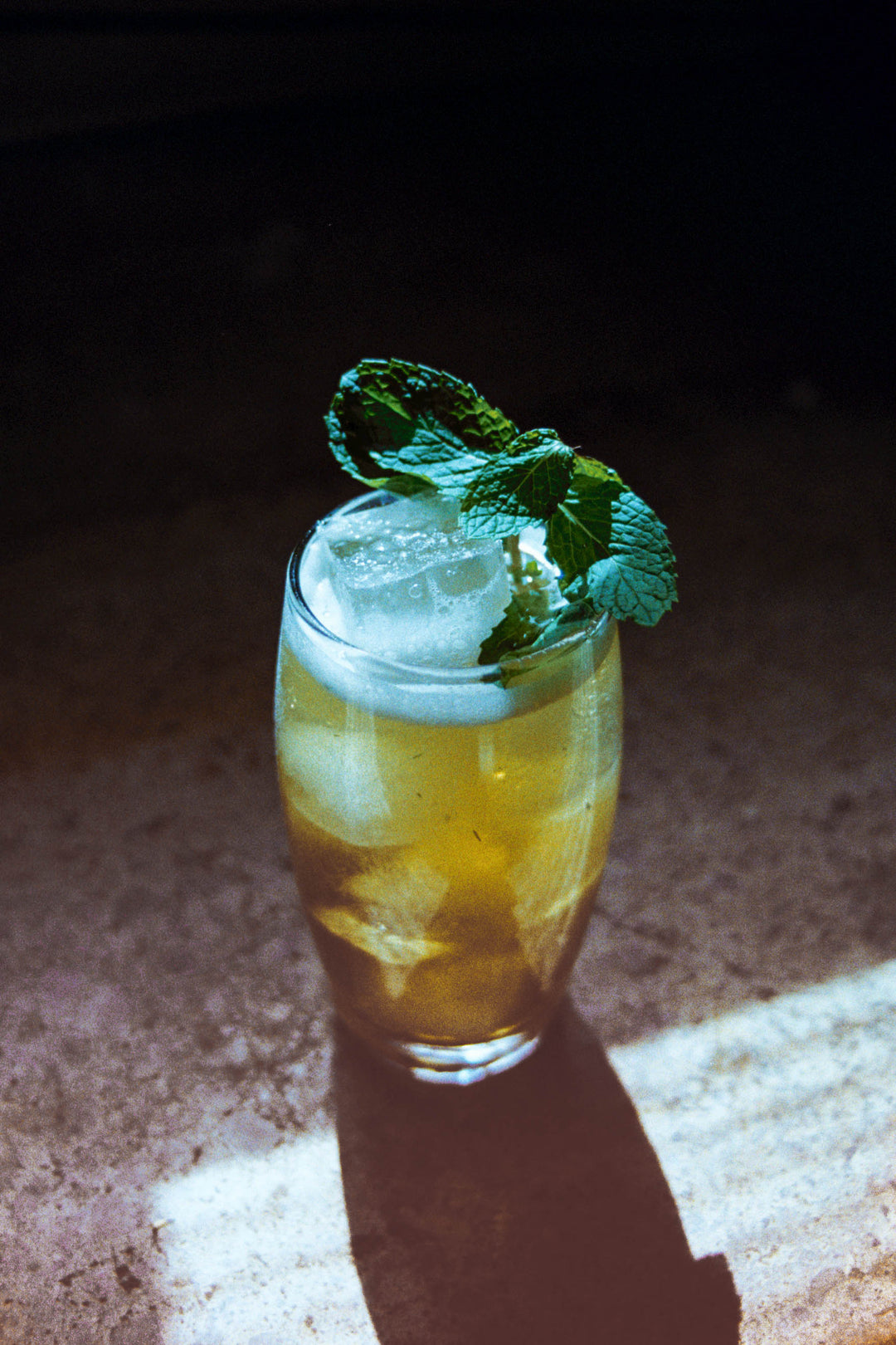 Boston Tea Derby cocktail in a highball glass filled with ice, garnish with mint on a wood table at a leather booth.
