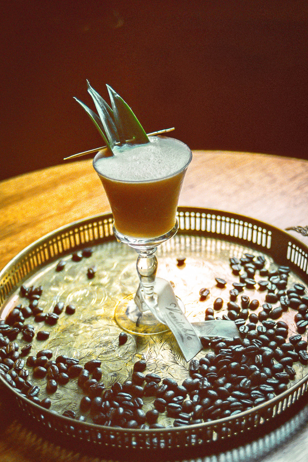 Image of Cafe Cabana cocktail, a tiki style cocktail using rum, coffee liqueur, velvet falernum, espresso, pineapple juice, cream of coconut and lemon juice.  Served in a tulip glass with pineapple leaf garnish.