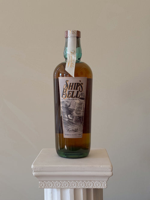 Bottle of 'Ship's Bell' bourbon on a white pedestal with a plain background