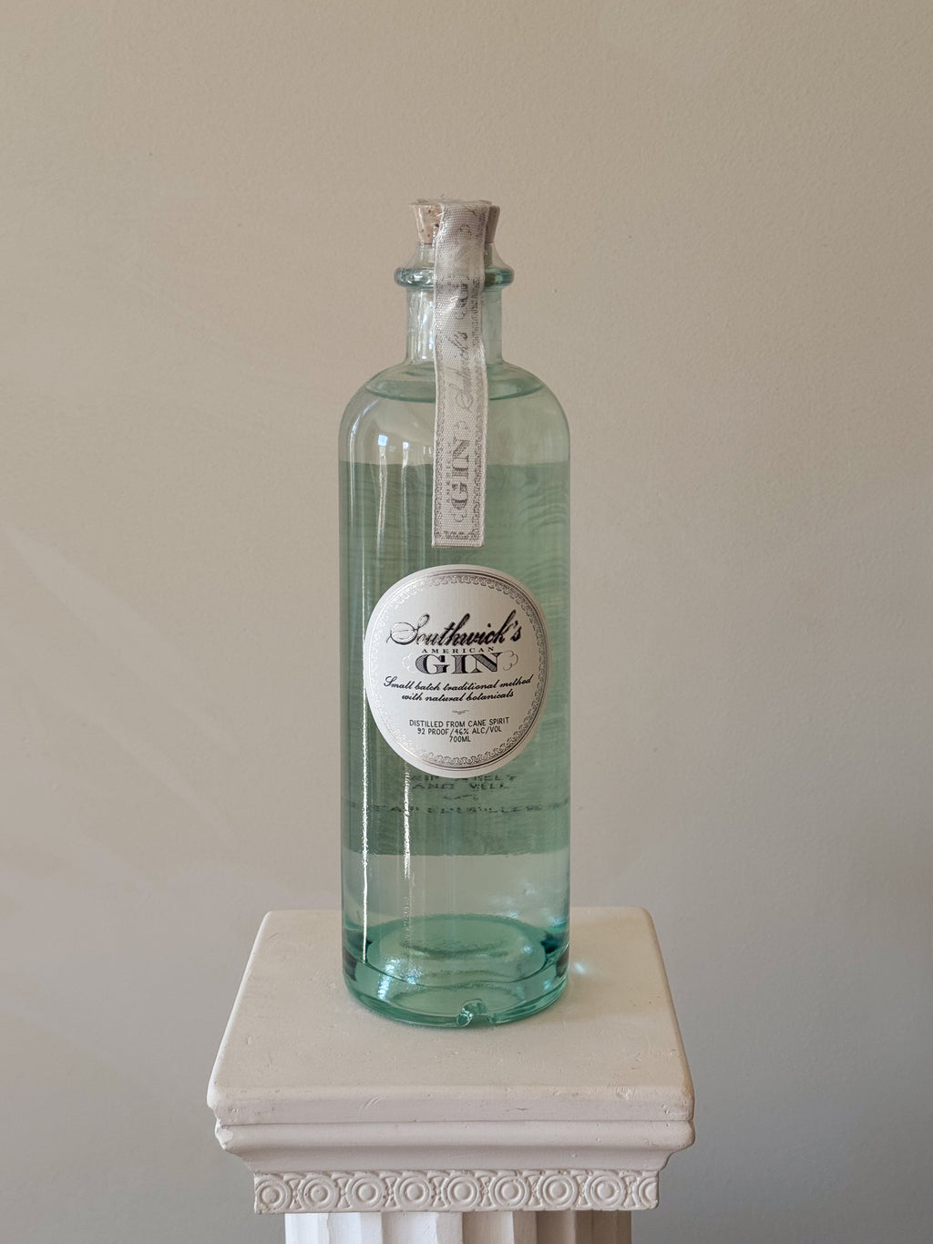 Bottle of 'Southwick's American Gin' on a white pedestal against a beige background
