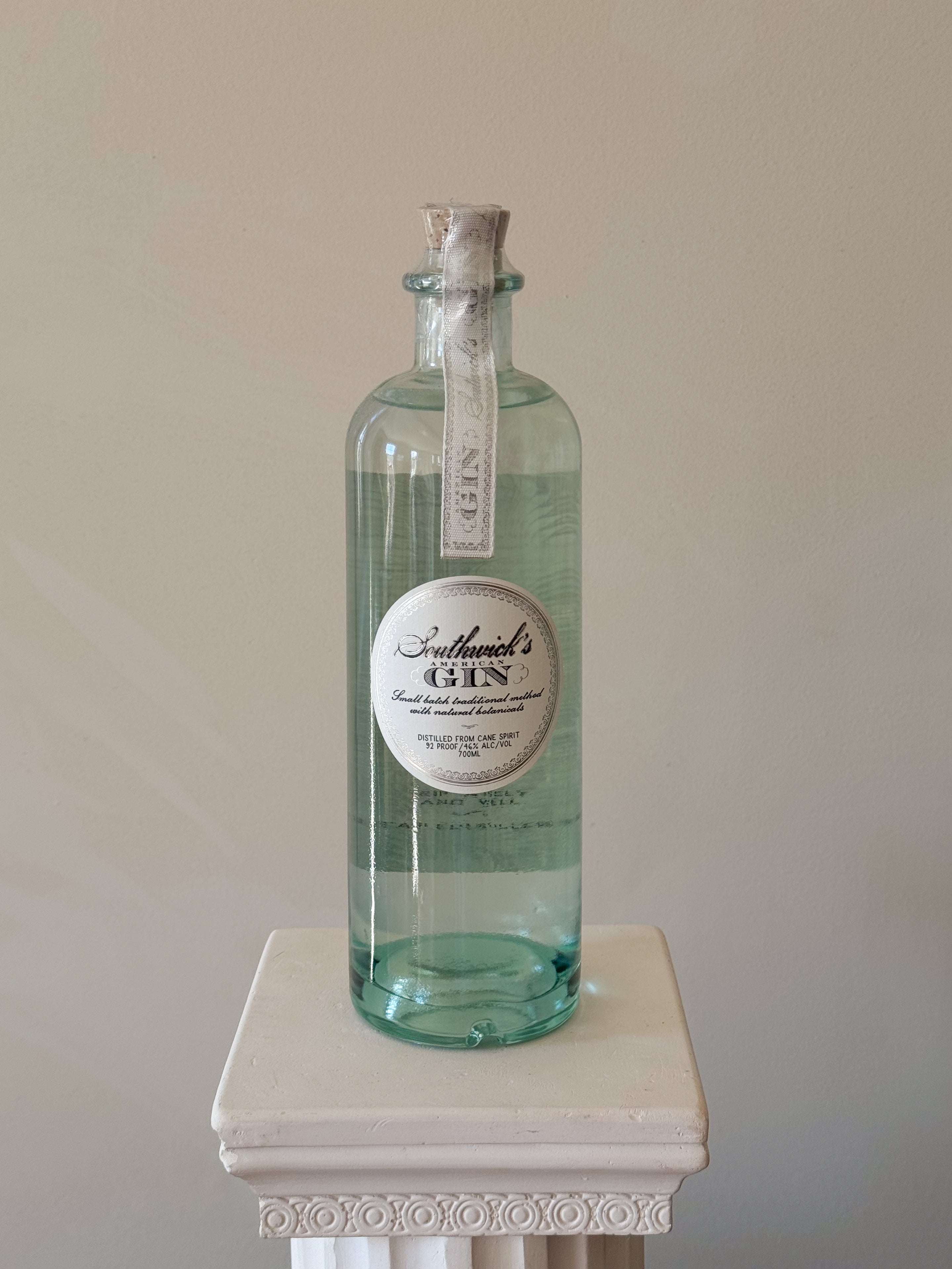 Bottle of 'Southwick's American Gin' on a white pedestal against a beige background