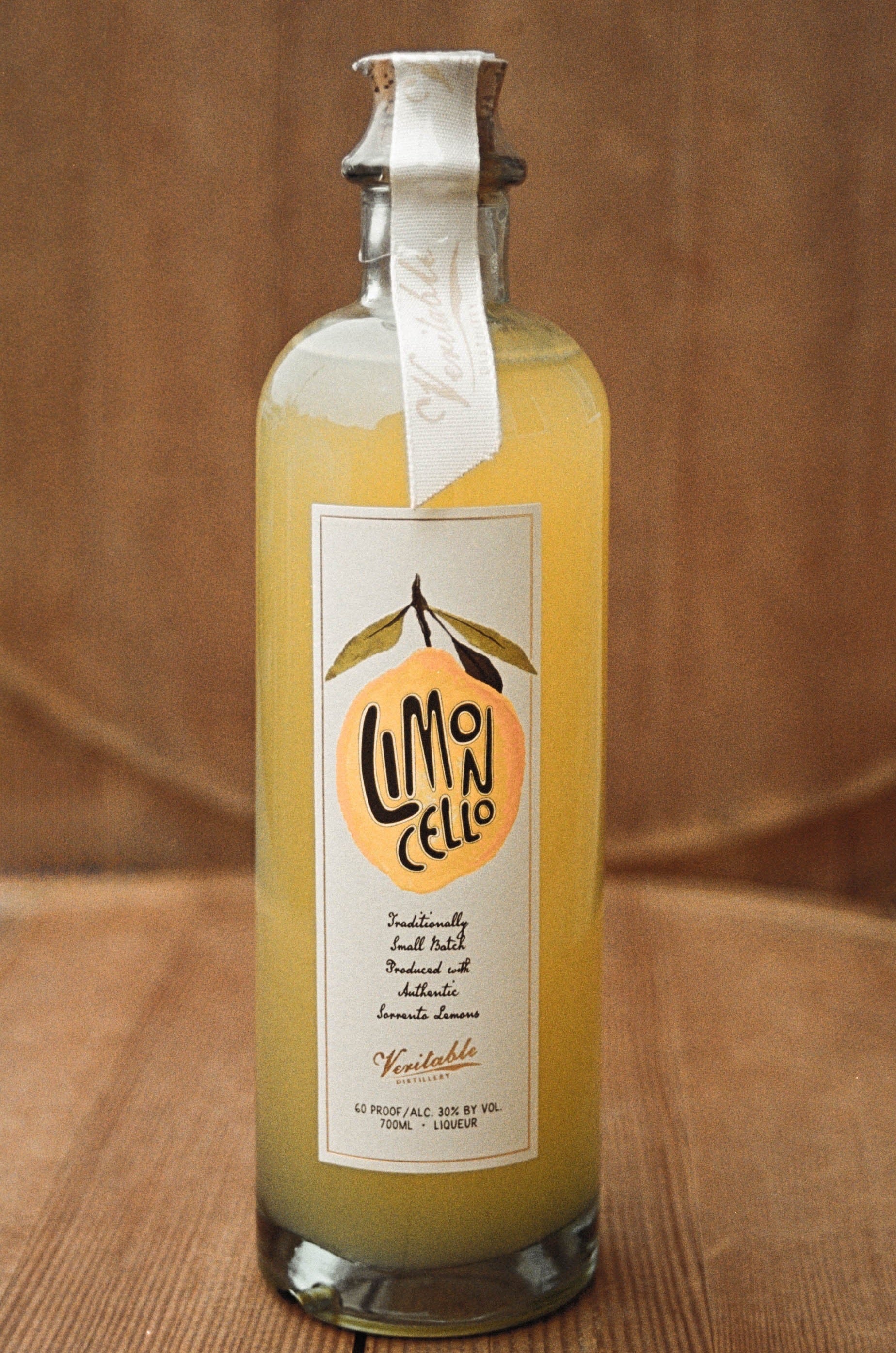 Image of bright yellow natural hand crafted Veritable Limoncello bottle on a wood background.