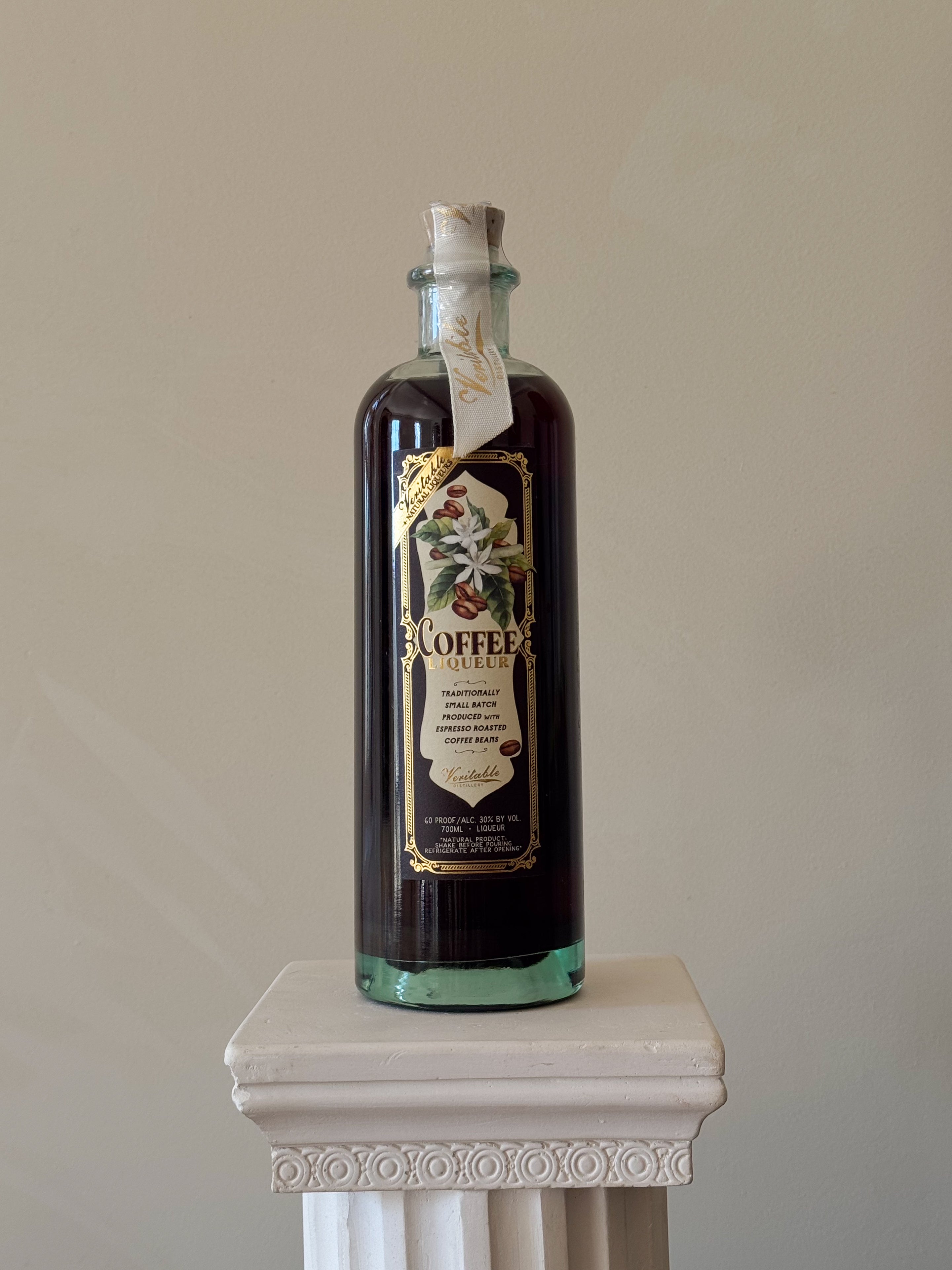 Bottle of 'Veritable Coffee Liqueur' on a white pedestal against a beige background